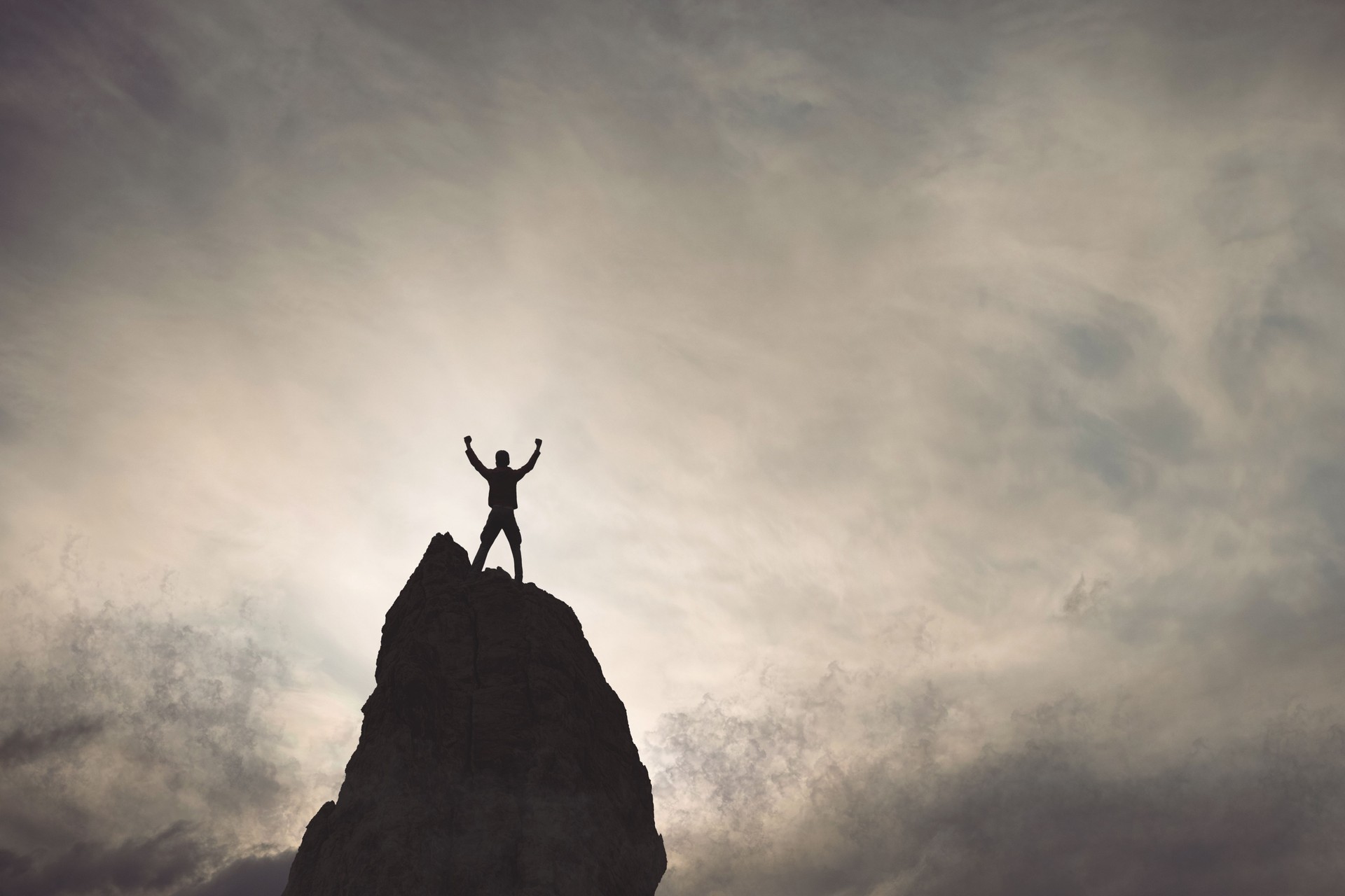 Silhouette of Triumphant Man on Mountain Peak at Sunset